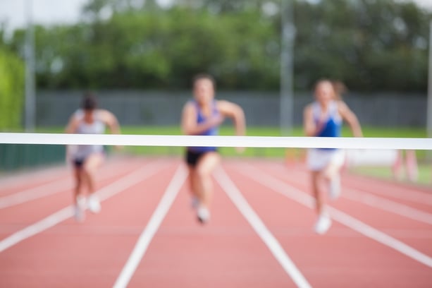 Female athletes running towards finish line on track field.jpeg