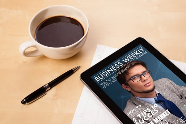 Workplace with tablet pc showing magazine cover and a cup of coffee on a wooden work table close-up.jpeg