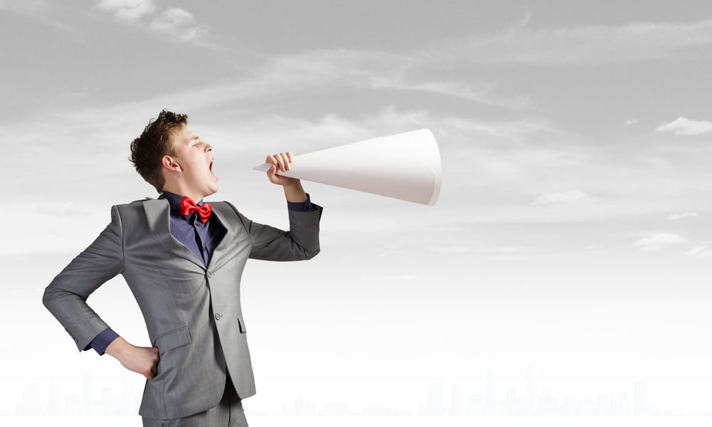 Young businessman screaming emotionally in paper trumpet